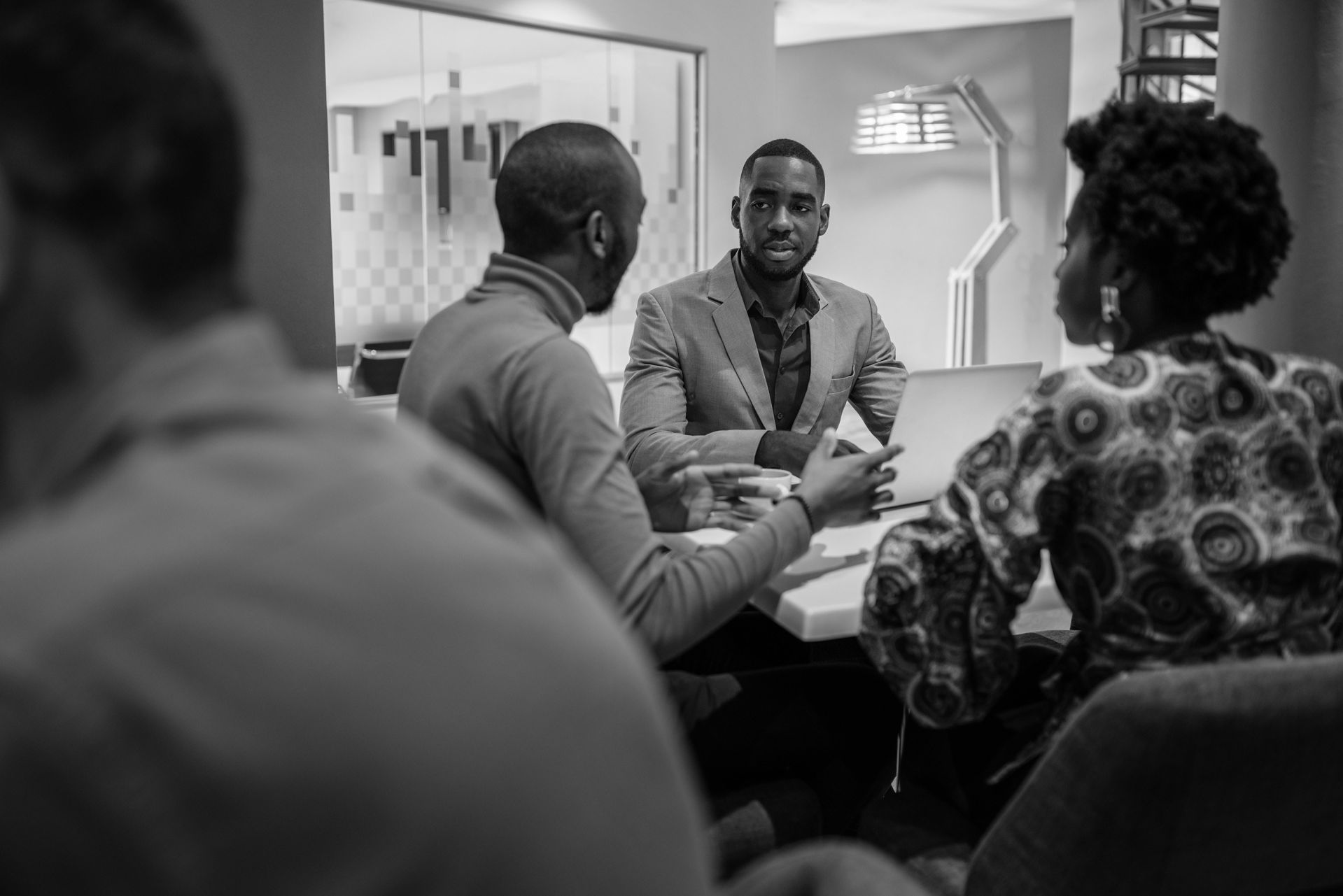 Three Black professionals in conversation at a table.